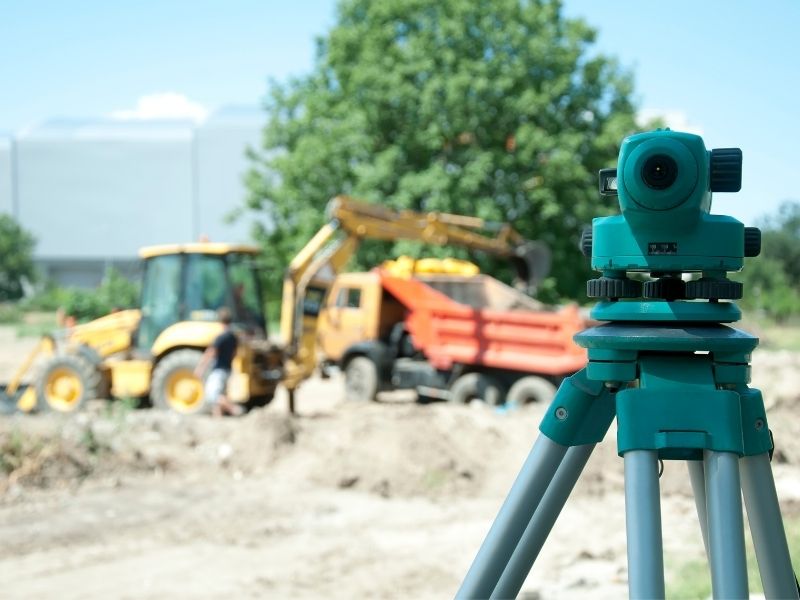 Surveying instrument on a construction site with excavation equipment in the background, illustrating boundary surveying to establish accurate property lines before new development.